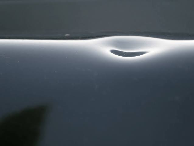 A single localized dent visible in reflected light on a dark vehicle panel