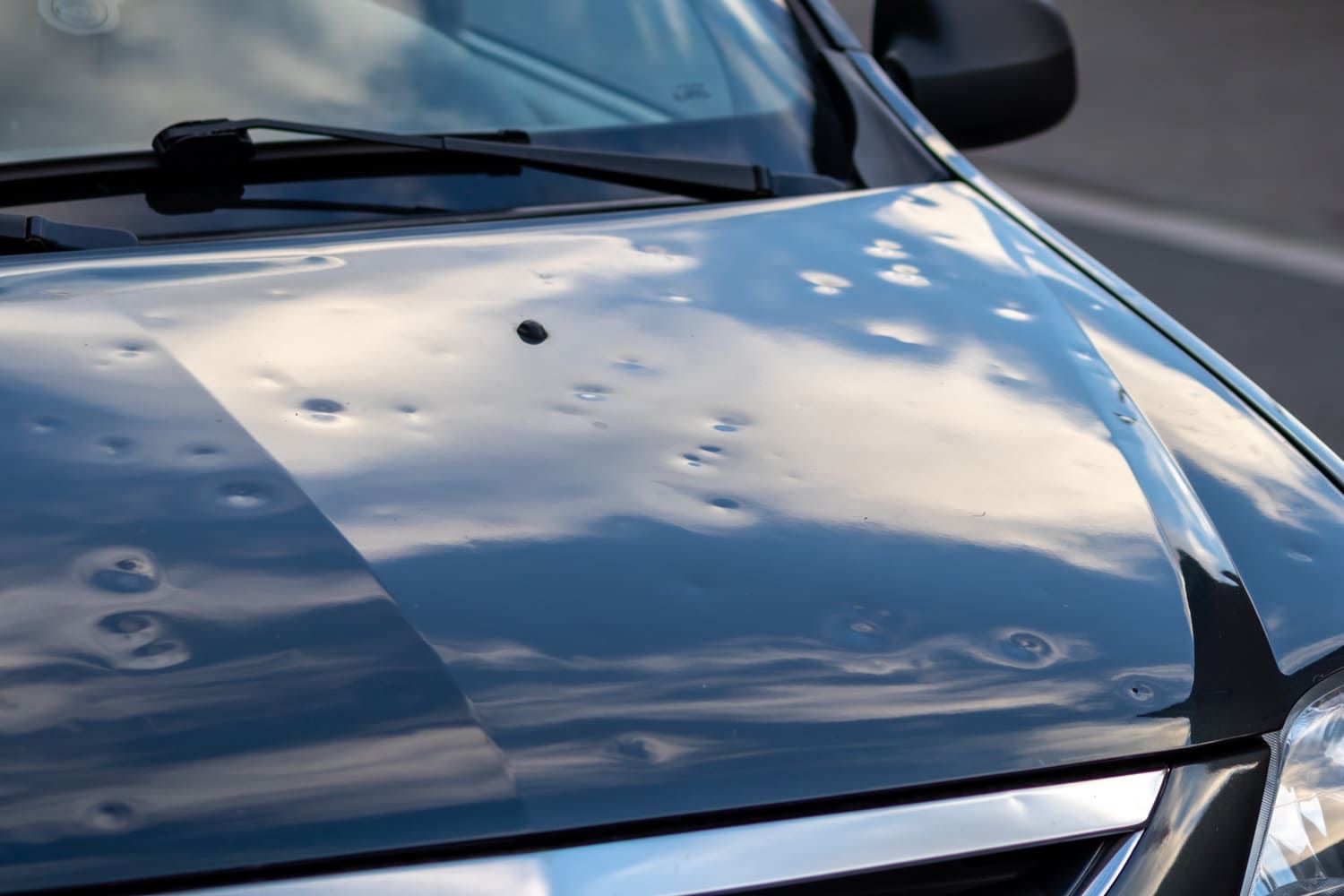 Numerous hail dents distributed across a dark vehicle hood